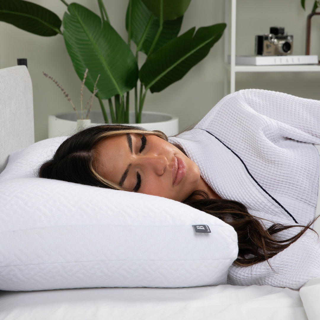 Woman sleeping on a white pillow with a plant and shelf in the background